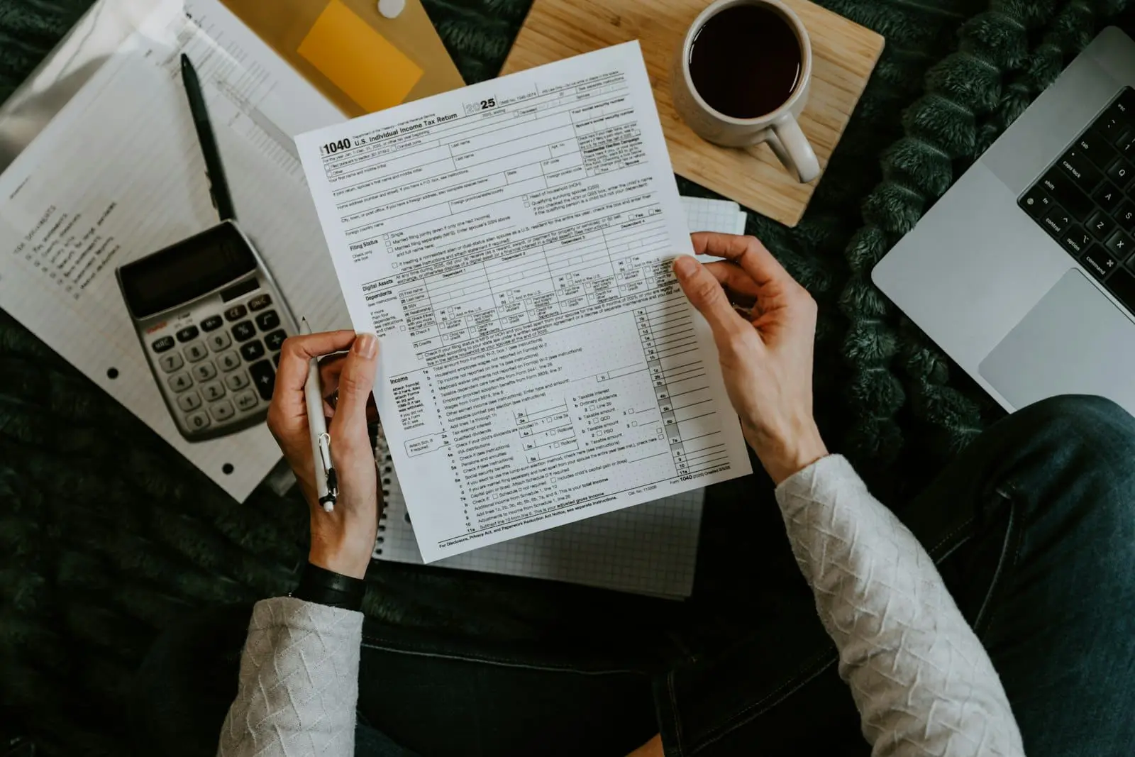 Hands holding tax documents alongside a calculator and laptop, illustrating the tax planning work behind a tax-loss harvesting strategy