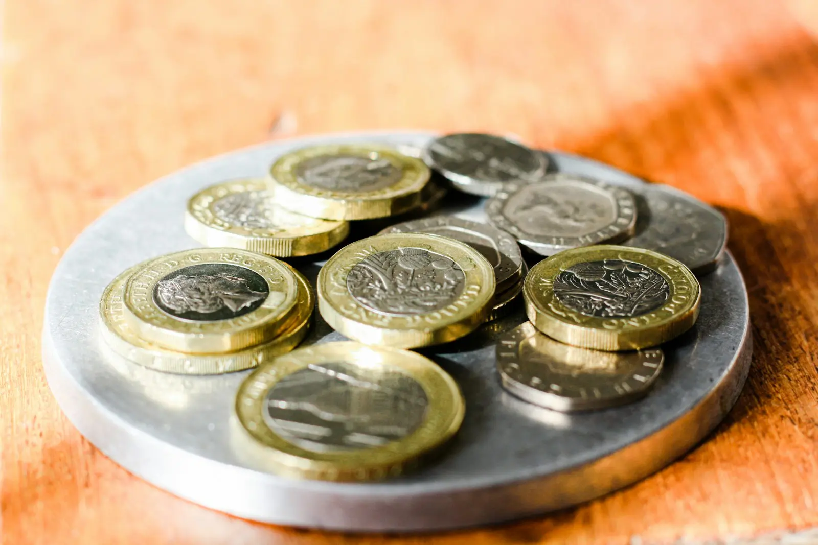UK pound and two pound coins with twenty pence and five pence pieces scattered on a table